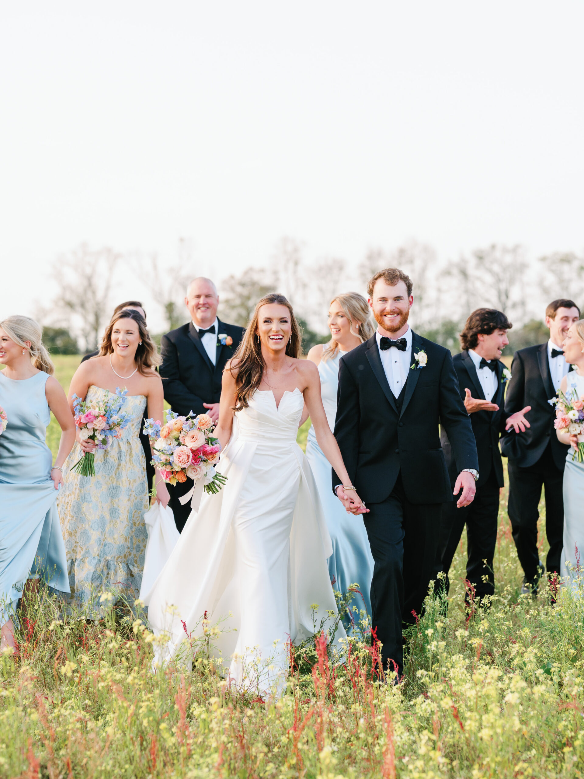 Bride and groom walking hand-in-hand with their wedding party through a wildflower field at Sundown Farms Plantation in Moultrie, Georgia